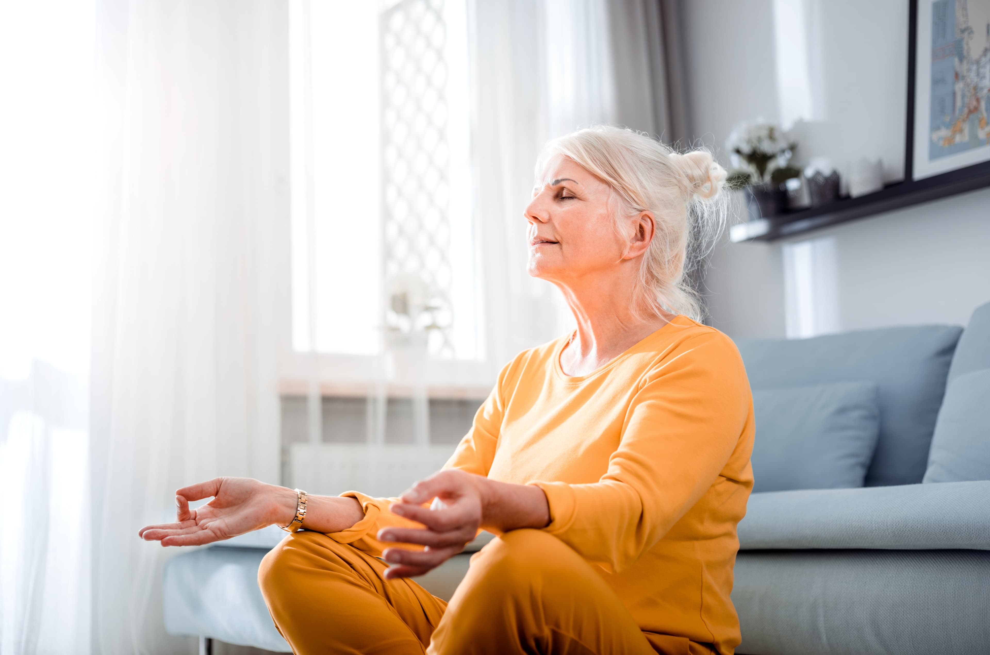 Senior female in lotus pose meditating sitting on floor at home